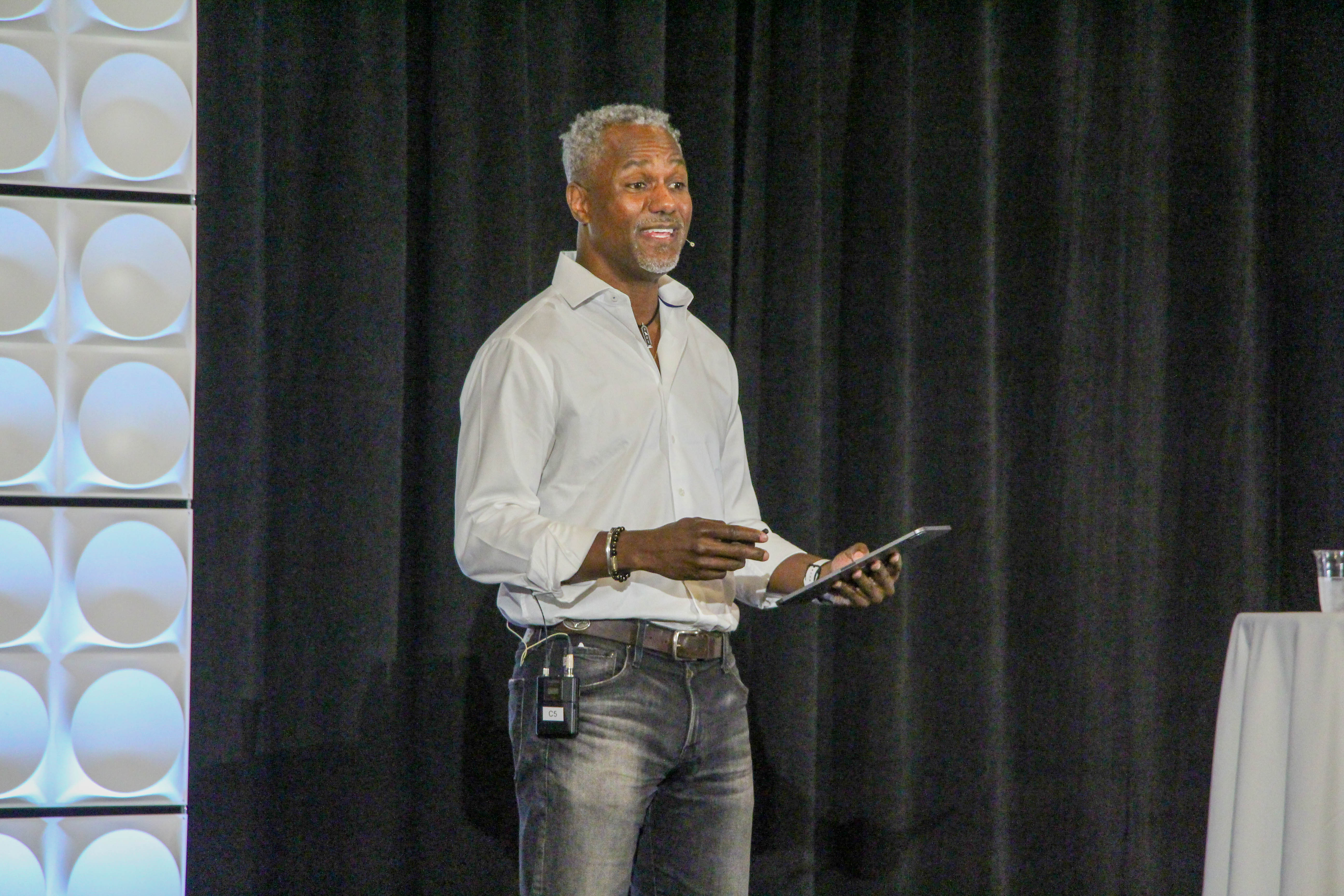 James presenting on stage, gesturing while holding a tablet